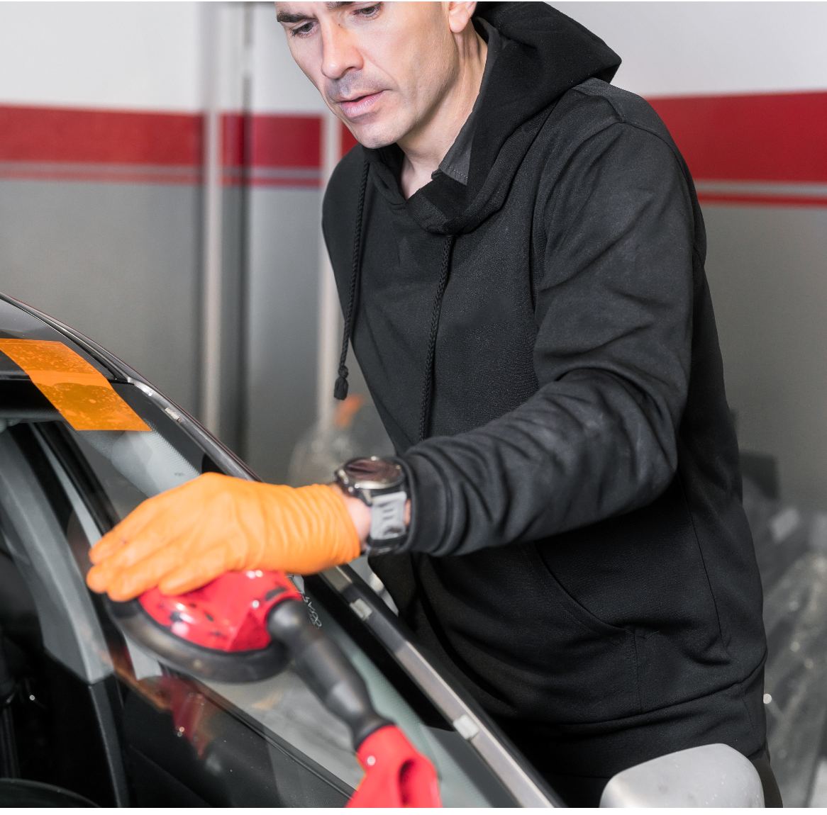 Professional man in black jacket applying window tint with orange gloves to car