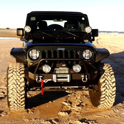 Black Jeep Wrangler lifted with oversized tires parked on desert sand