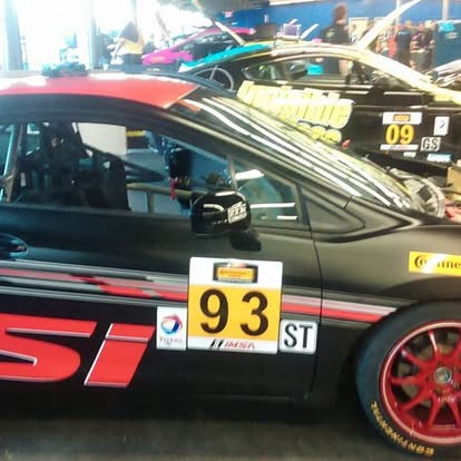 Red race car with number 93 plate displayed at auto show with other vehicles visible in background