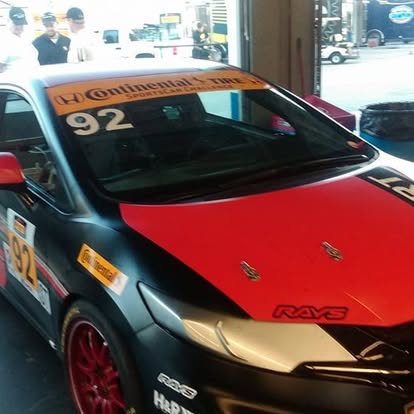 Race car with red and black hood displayed in dealership showroom