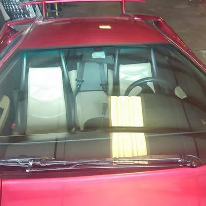 Red vintage car interior viewed through windshield showing steering wheel and tan seats