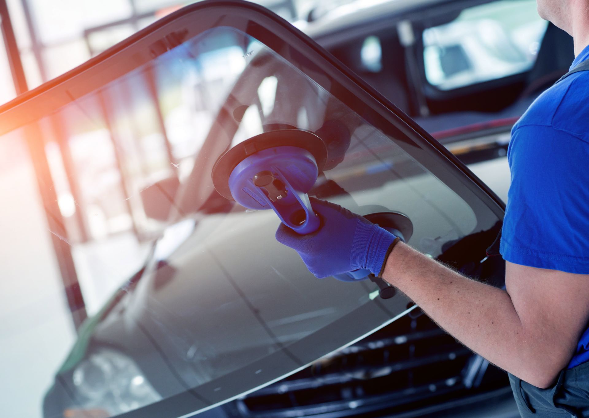 Technician in blue gloves applying protective film to car window with squeegee tool