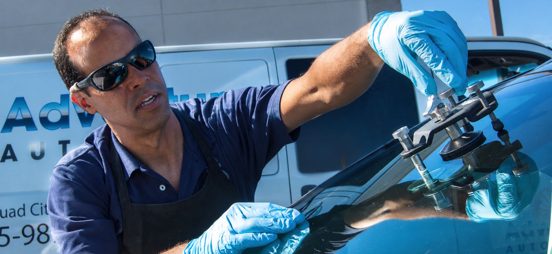 Professional technician in blue gloves using spray equipment on windshield