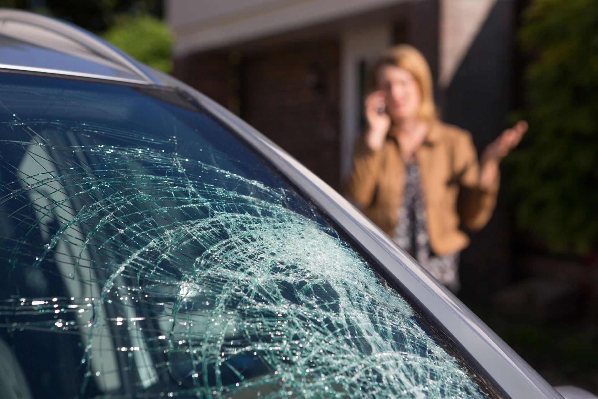 Shattered windshield of blue car with blurred person in background