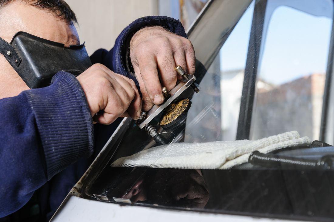 Worker in blue sweater using scraper tool on window glass outdoors