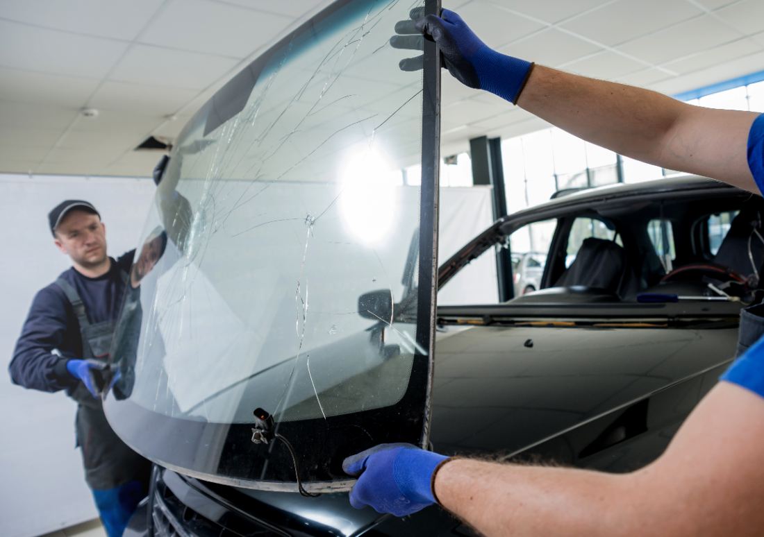 Technicians installing new windshield on vehicle in auto service shop